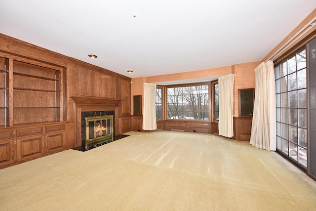 unfurnished living room with wooden walls, plenty of natural light, a premium fireplace, and light carpet