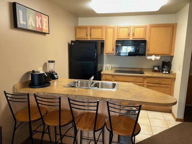 kitchen with light tile patterned flooring, a breakfast bar, sink, black appliances, and light brown cabinets