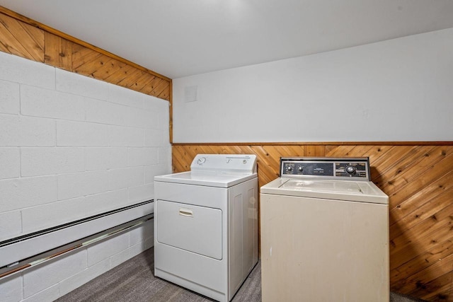 clothes washing area featuring a baseboard heating unit, washing machine and clothes dryer, dark carpet, and wood walls