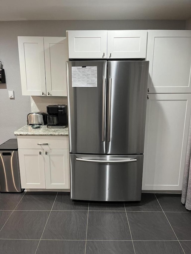 kitchen with light stone countertops, white cabinets, stainless steel refrigerator, and dark tile patterned flooring