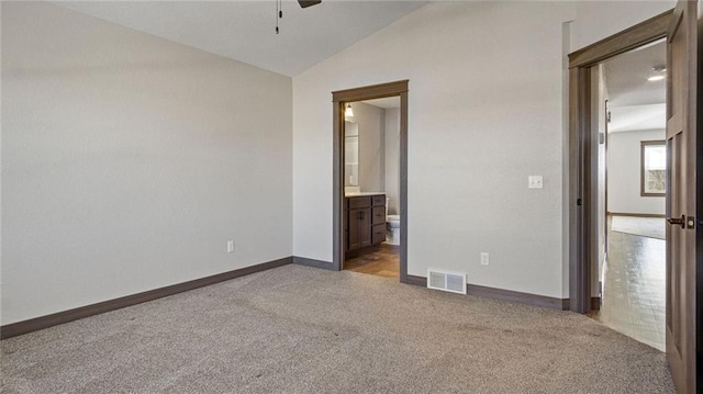 unfurnished bedroom with light carpet, ensuite bath, and vaulted ceiling