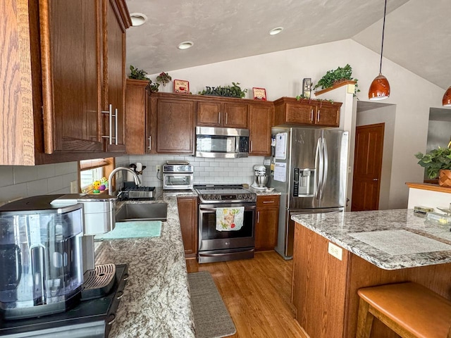 kitchen featuring lofted ceiling, sink, hanging light fixtures, light stone counters, and stainless steel appliances