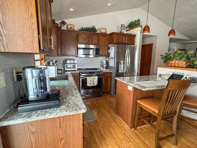 kitchen with light stone counters, hanging light fixtures, light hardwood / wood-style flooring, appliances with stainless steel finishes, and a kitchen island