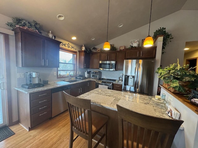 kitchen featuring pendant lighting, stainless steel appliances, light stone countertops, and dark brown cabinets