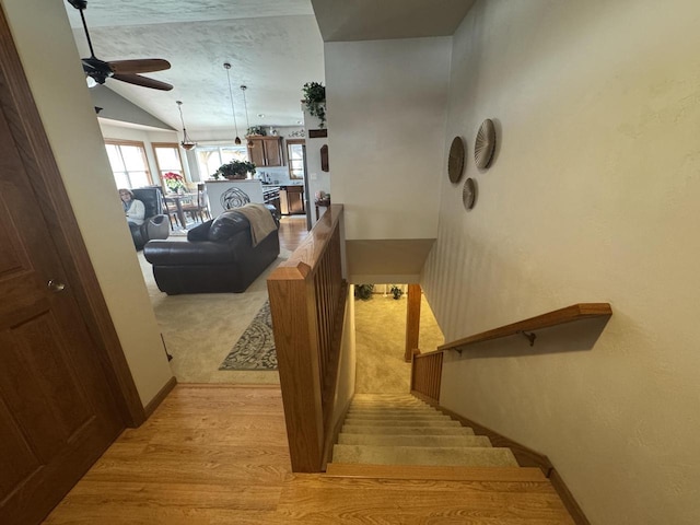 stairway with ceiling fan, wood-type flooring, and vaulted ceiling