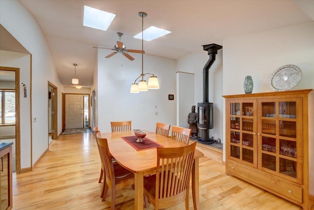 dining area featuring light hardwood / wood-style flooring, lofted ceiling with skylight, and a wood stove