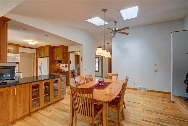 dining room with ceiling fan, vaulted ceiling with skylight, and light wood-type flooring