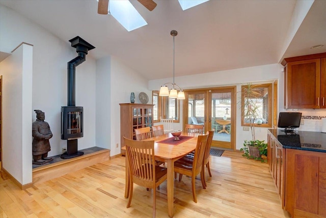 dining space with light wood-type flooring, lofted ceiling with skylight, french doors, and a wood stove