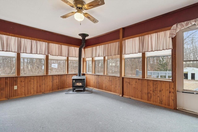 unfurnished sunroom featuring a wood stove and ceiling fan