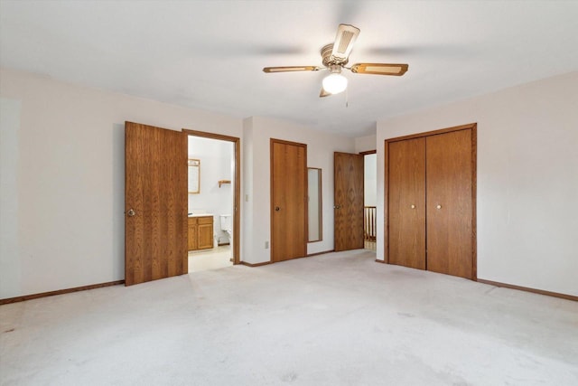 unfurnished bedroom featuring two closets, light colored carpet, ceiling fan, and ensuite bathroom