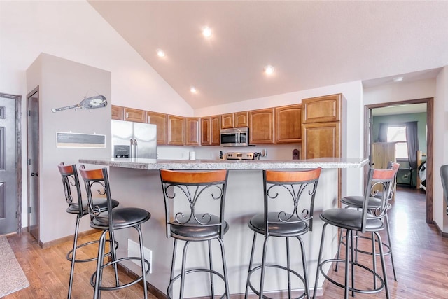 kitchen featuring a breakfast bar area, stainless steel appliances, a center island, high vaulted ceiling, and light hardwood / wood-style floors