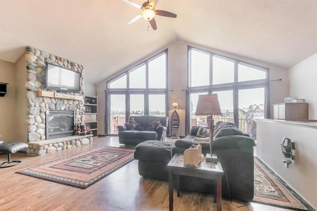 living room featuring a stone fireplace, wood-type flooring, high vaulted ceiling, and ceiling fan