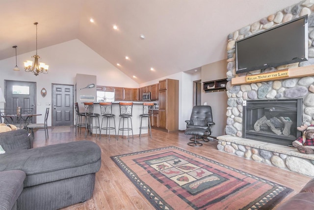 living room with wood-type flooring, a stone fireplace, high vaulted ceiling, and an inviting chandelier