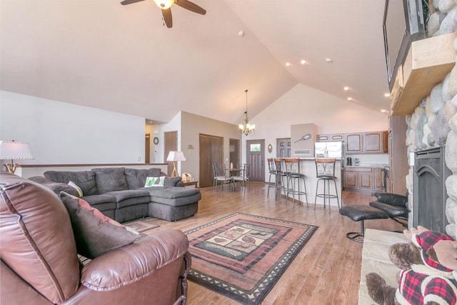 living room featuring ceiling fan with notable chandelier, high vaulted ceiling, and light hardwood / wood-style flooring