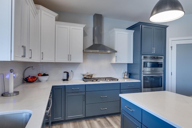 kitchen with appliances with stainless steel finishes, blue cabinetry, white cabinets, and wall chimney exhaust hood