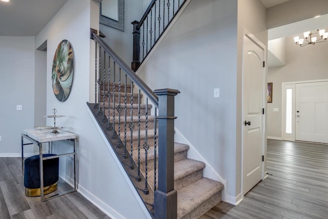 stairs with an inviting chandelier, a towering ceiling, and hardwood / wood-style floors