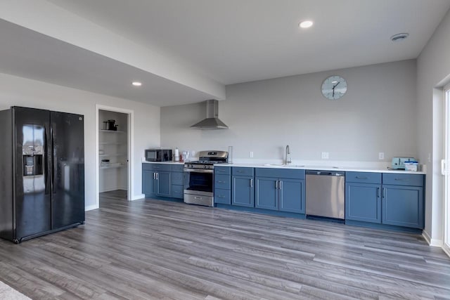 kitchen featuring hardwood / wood-style floors, sink, black appliances, blue cabinetry, and wall chimney range hood