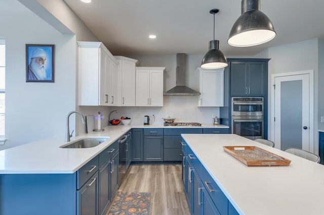 kitchen featuring sink, appliances with stainless steel finishes, white cabinets, blue cabinets, and wall chimney exhaust hood