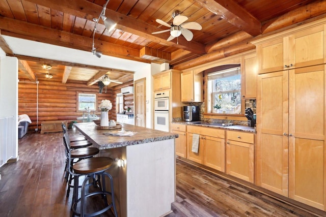 kitchen featuring dark wood-type flooring, double oven, a kitchen island, light brown cabinetry, and wooden ceiling