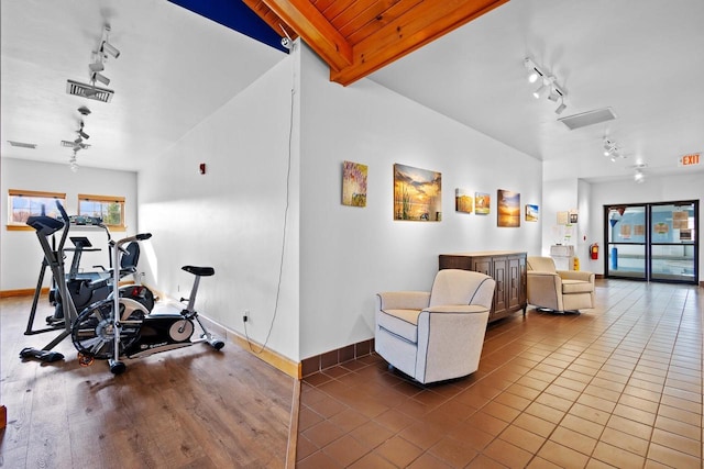 exercise room with tile patterned flooring, vaulted ceiling, and track lighting