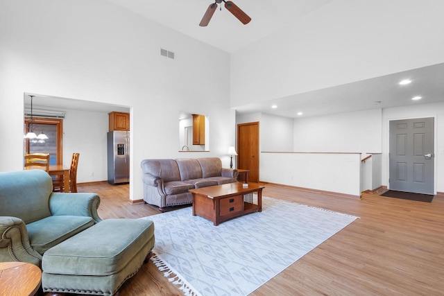 living room with a high ceiling, ceiling fan with notable chandelier, and light wood-type flooring