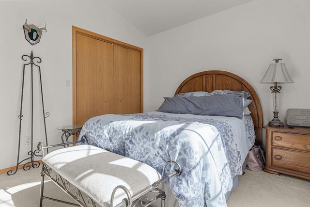 bedroom with vaulted ceiling, light colored carpet, and a closet