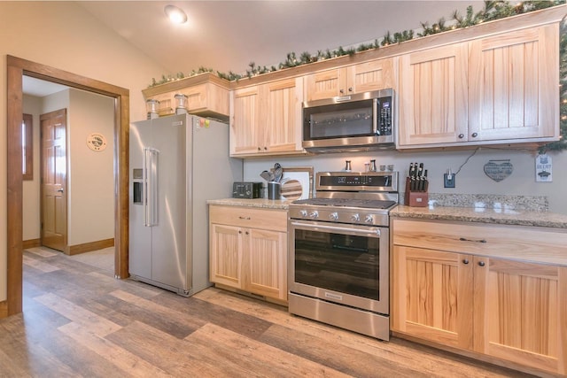 kitchen featuring lofted ceiling, light brown cabinetry, appliances with stainless steel finishes, light stone countertops, and light hardwood / wood-style floors