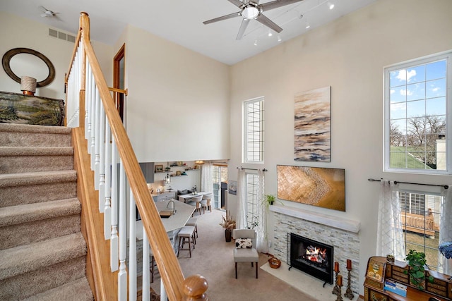 living room with ceiling fan, a fireplace, carpet, and a high ceiling