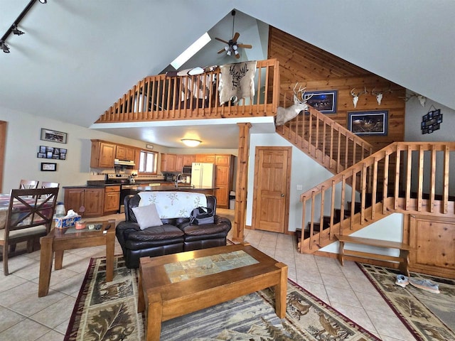 living room featuring light tile patterned floors, ceiling fan, high vaulted ceiling, track lighting, and wood walls