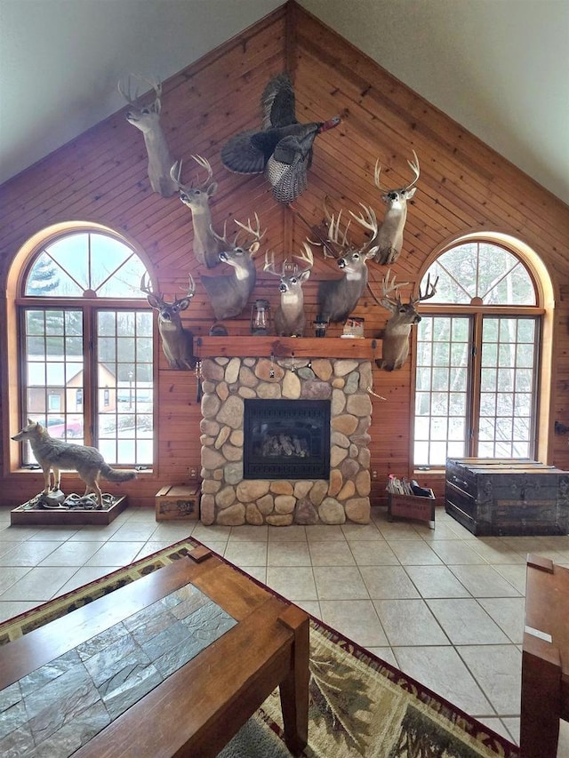 living room featuring a stone fireplace, high vaulted ceiling, and wood walls