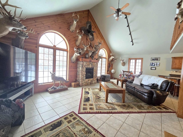 living room featuring wooden walls, a stone fireplace, high vaulted ceiling, and light tile patterned floors