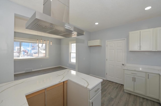 kitchen featuring white cabinetry, light stone countertops, pendant lighting, and island range hood