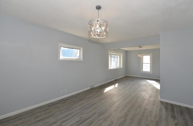 unfurnished room featuring an inviting chandelier, dark hardwood / wood-style flooring, and a textured ceiling