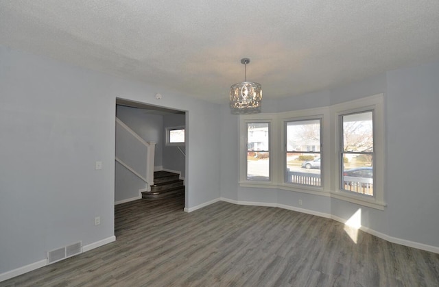 empty room featuring dark wood-type flooring, a chandelier, and a textured ceiling