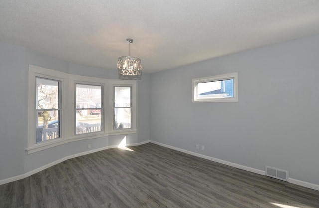 spare room featuring an inviting chandelier, dark wood-type flooring, and a textured ceiling