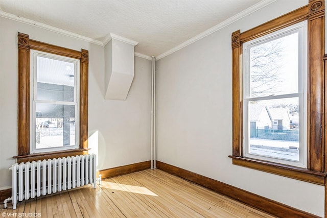 empty room with light hardwood / wood-style flooring, radiator, crown molding, and a wealth of natural light