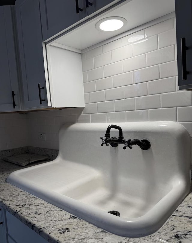 interior details featuring light stone counters, sink, decorative backsplash, and blue cabinets