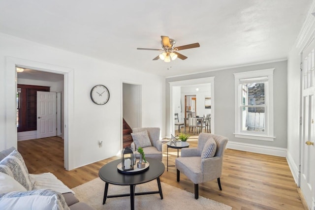 living room featuring baseboards, light wood-style flooring, ceiling fan, stairway, and crown molding