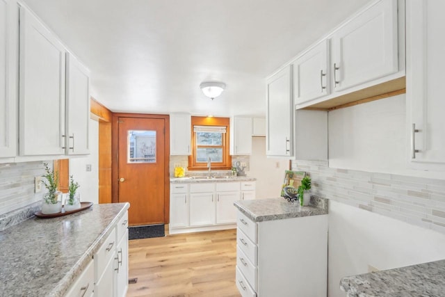 kitchen with light wood-style flooring, backsplash, light stone countertops, white cabinetry, and a sink