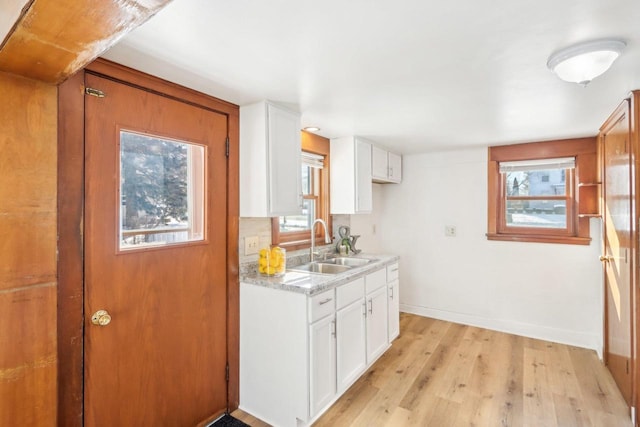 kitchen featuring light wood-type flooring, white cabinetry, light countertops, and a sink