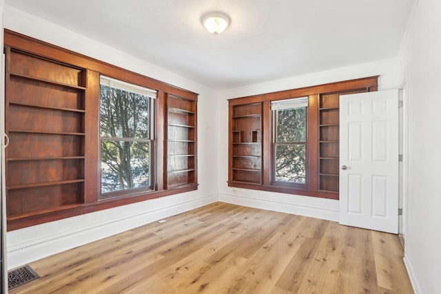 interior space with light wood-style floors, a healthy amount of sunlight, visible vents, and baseboards