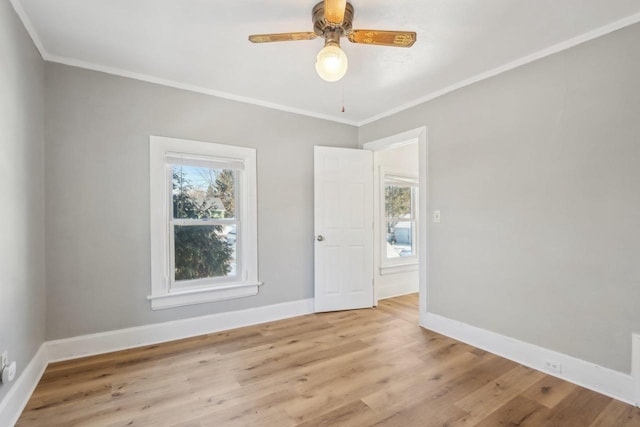 empty room featuring crown molding, light wood-style flooring, and baseboards