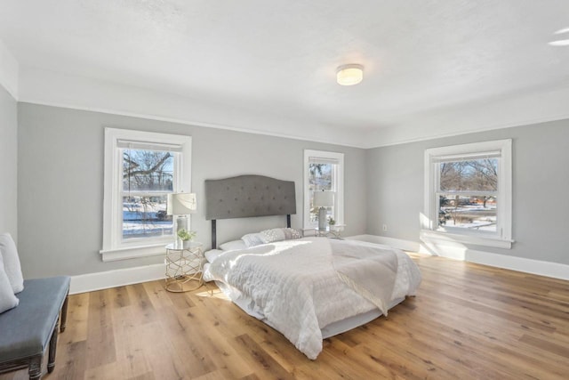 bedroom with multiple windows, light wood-type flooring, and baseboards