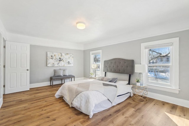 bedroom with multiple windows, light wood-type flooring, and baseboards