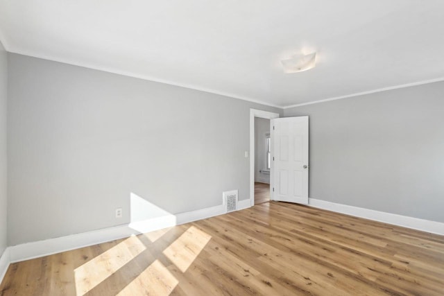 empty room featuring baseboards, crown molding, visible vents, and wood finished floors