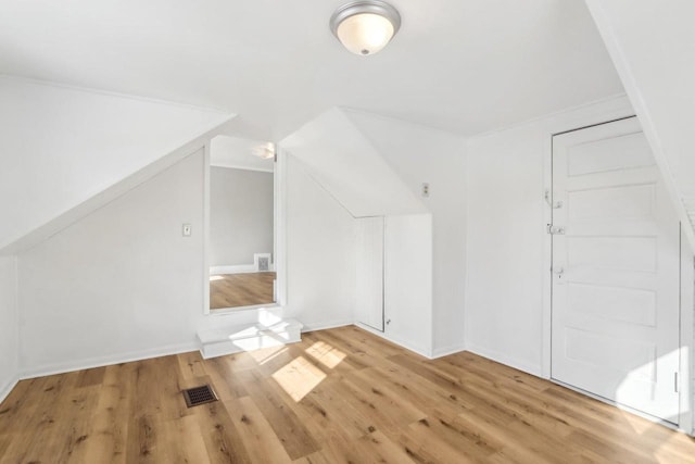 additional living space featuring vaulted ceiling, light wood finished floors, visible vents, and baseboards