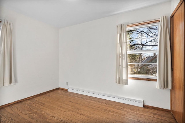 spare room featuring a baseboard heating unit, baseboards, and wood finished floors