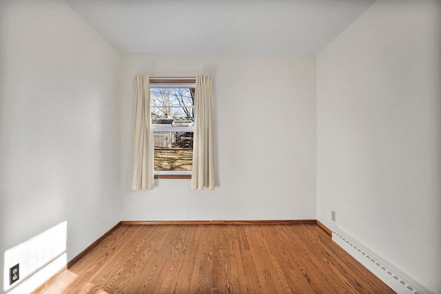 empty room featuring baseboards, baseboard heating, and wood finished floors