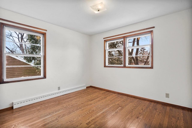 empty room with wood finished floors, a healthy amount of sunlight, baseboards, and baseboard heating