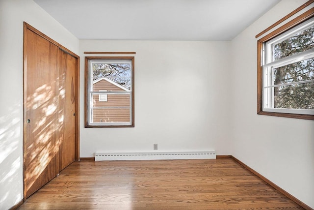 spare room with a healthy amount of sunlight, a baseboard heating unit, baseboards, and wood finished floors